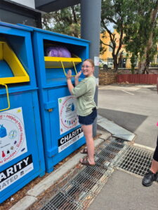 Person donating clothes at charity bin in Australia.