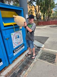 Child donating stuffed toy to charity bin.