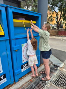 Mother and child donating clothes at charity bin.